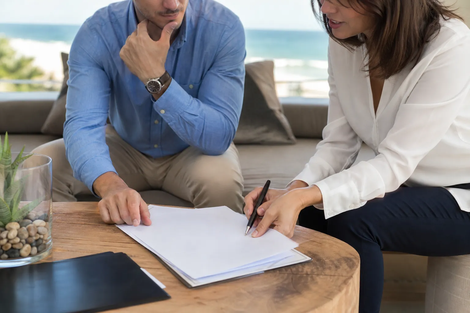 A man and woman review a blank document together at a table in a bright coastal office.