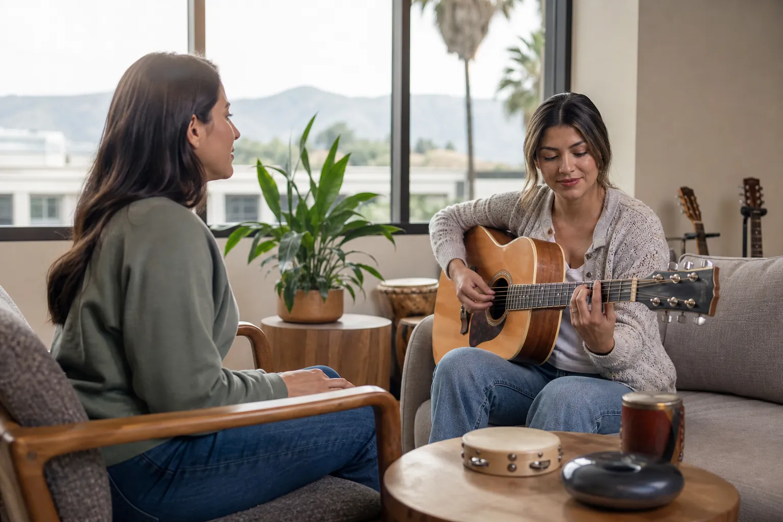 Woman Playing Guitar in a Music Therapy Session A woman plays an acoustic guitar for another woman in a calm room with percussion instruments nearby.
