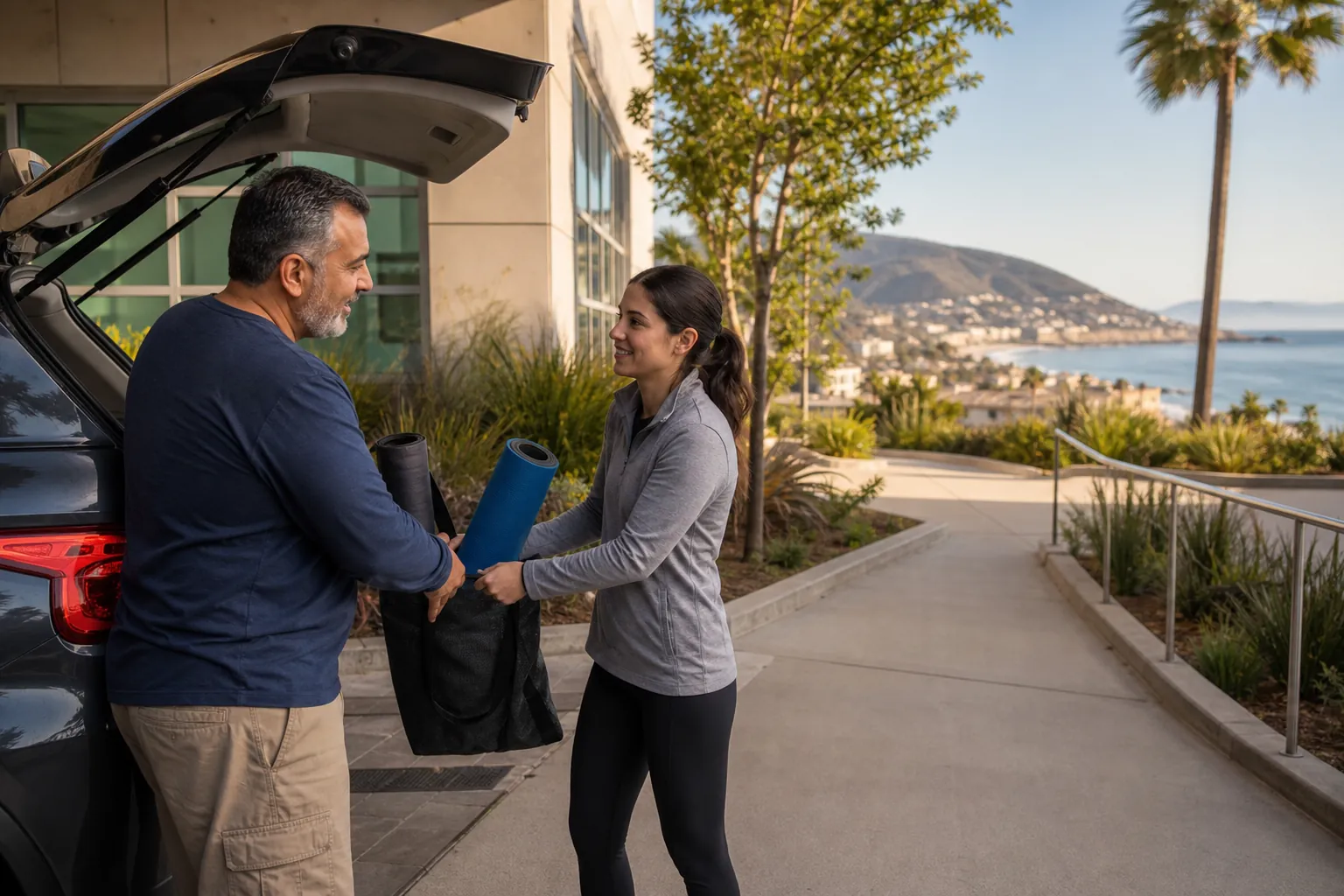 Transferring Exercise Gear Outside a Coastal Rehab Facility A man and woman load rolled exercise mats into a bag beside an open car outside a coastal rehabilitation facility.